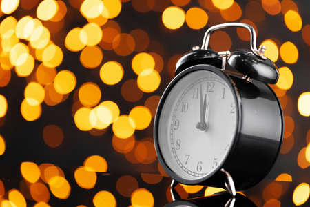 New Year eve concept with alarm clock against blurred garland