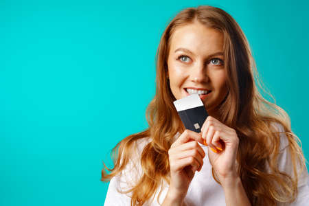 Smiling young woman biting a credit card within temptation of shopping