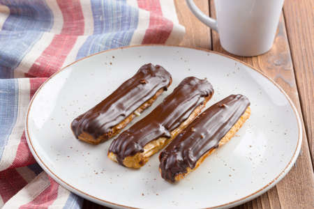 Chocolate eclairs on white plate on wooden table