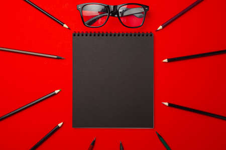 Black pencils and glasses on red background top view