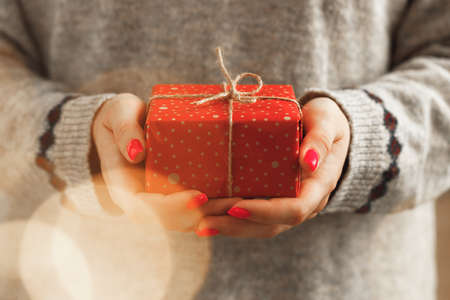 Female hands in sweater holding wrapped Christmas giftの写真素材