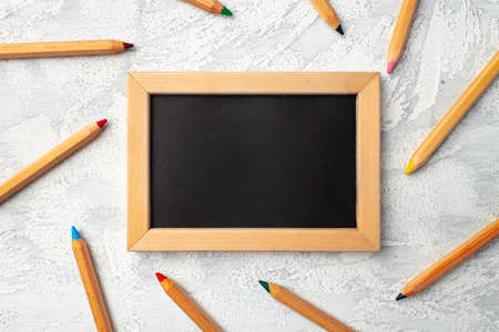 Small blackboard in wooden frame surrounded by color pencilsの写真素材