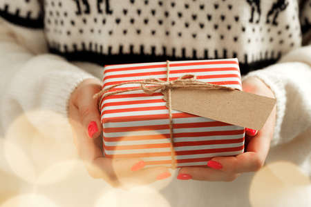 Female hands in sweater holding wrapped Christmas giftの写真素材