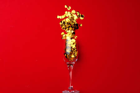 Champagne glass with glitter confetti on red background flat layの写真素材