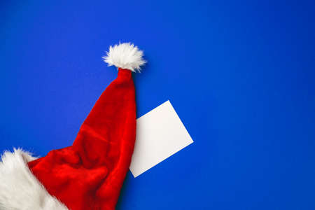 Blank paper sheet and Snata Claus hat on blue backgroundの写真素材