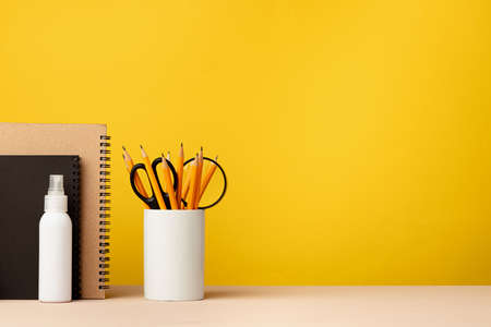 Cup of pencils and notepads on desk against yellow background