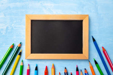 Small blackboard in wooden frame surrounded by color pencilsの写真素材