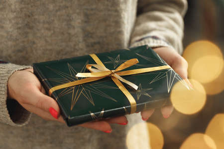 Female hands in sweater holding wrapped Christmas giftの写真素材