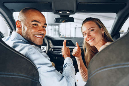 Joyful young couple looking around inside a new car they are going to buy in a car shop