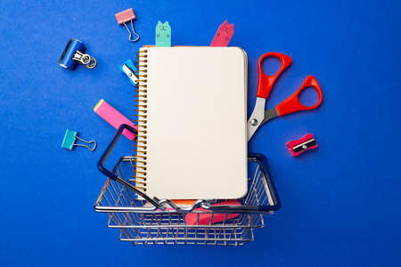 School supplies in a shopping cart on blue background