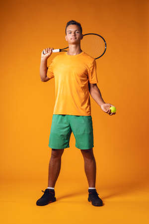 Full-length portrait of a tennis player man in action against orange backgroundの写真素材
