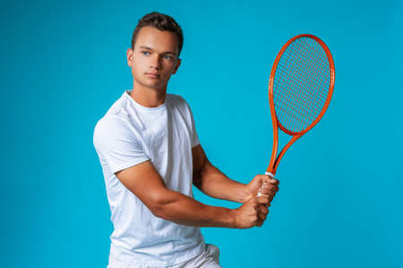 Young man tennis player in sportswear posing against blue backgroundの写真素材