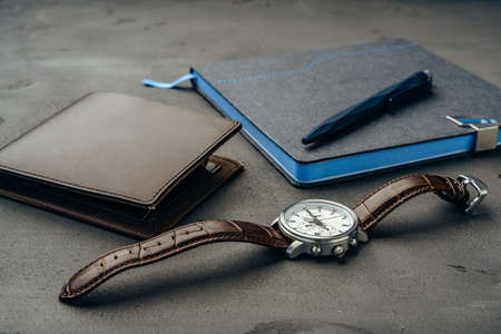 Businessmans accessories including notepad, watch and purse on dark grey background