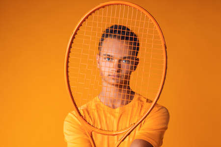 Studio shot of a young tennis player holding racket against orange backgroundの写真素材