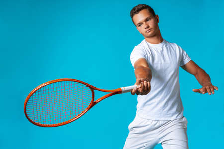 Young man tennis player in sportswear posing against blue backgroundの写真素材