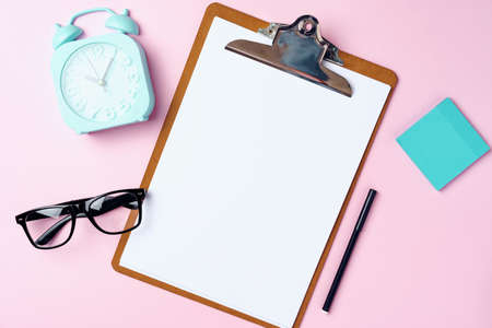 Clipboard with blank sheet of paper and alarm clock on pinkの写真素材