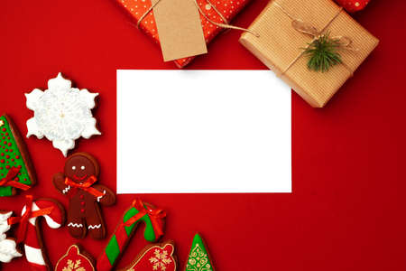 Blank sheet of paper with Christmas gift and gingerbread cookies on red backgroundの写真素材