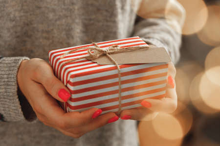 Female hands in sweater holding wrapped Christmas giftの写真素材