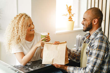 Smiling blonde woman talking to a waiter of a coffee shop at the counter