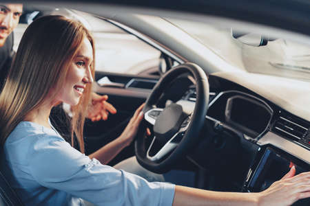 Attractive young woman sitting in new car in showroom