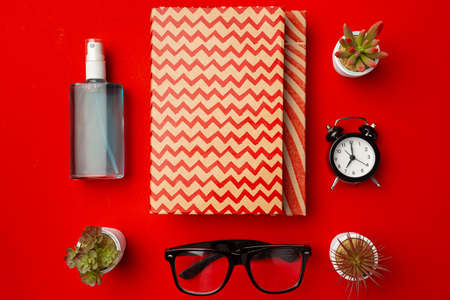 Closed notepad with glasses, flower pots and hand sanitizer on red backgroundの写真素材