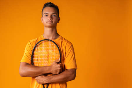 Studio shot of a young tennis player holding racket against orange backgroundの写真素材