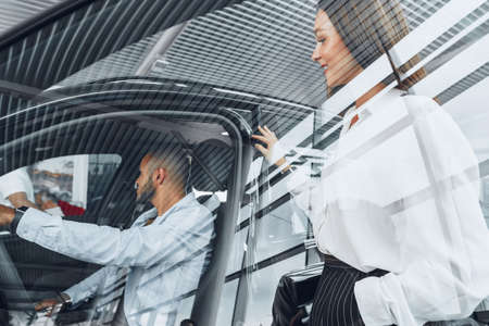 Young attractive woman salesperson in car showroom showing a car to her male client