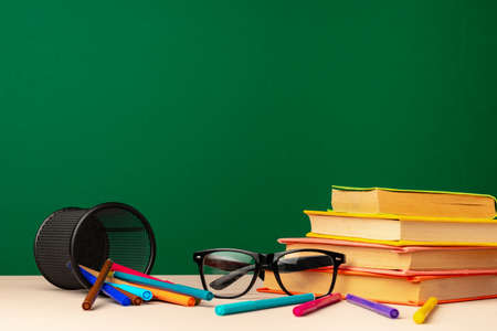 School supplies on wooden desk against green chalkboardの写真素材