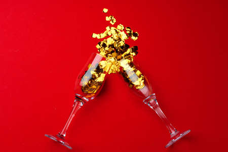 Champagne glass with glitter confetti on red background flat layの写真素材