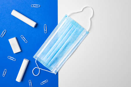 Pieces of chalk, paper clips and medical mask on blue and white backgroundの写真素材