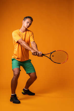 Full-length portrait of a tennis player man in action against orange background