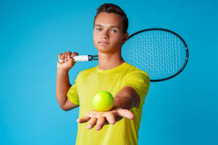 Young man tennis player in sportswear posing against blue backgroundの写真素材
