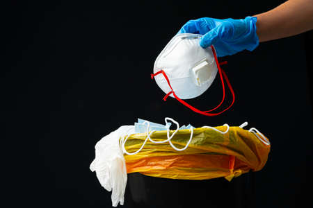 Hand putting used dirty surgical mask to a garbage bin.