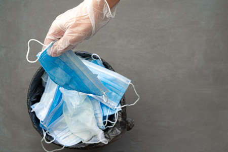 Hand putting used dirty surgical mask to a garbage bin.