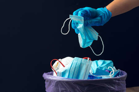 Hand putting used dirty surgical mask to a garbage bin.の写真素材