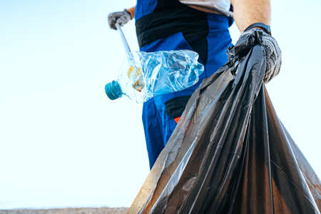 Hand of a man volunteer grabbing plastic litter into a waste bag cleaning up the beach