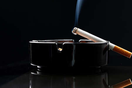 Burning cigarette in a black ash trayの写真素材