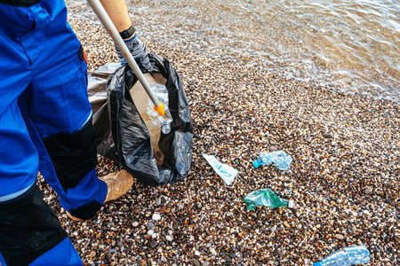 Close up photo of a man collecting garbage with a grabbing tool on the beach