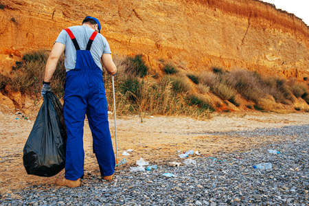 Man volunteer collecting garbage on the beach with a reach extender stick