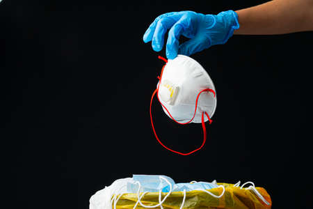 Hand putting used dirty surgical mask to a garbage bin.