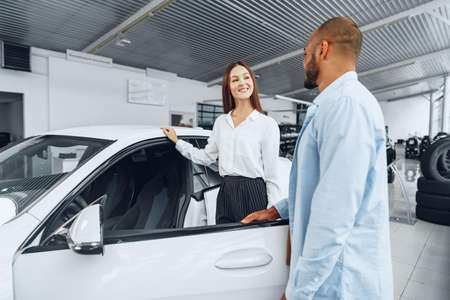 Young attractive woman salesperson in car showroom showing a car to her male client