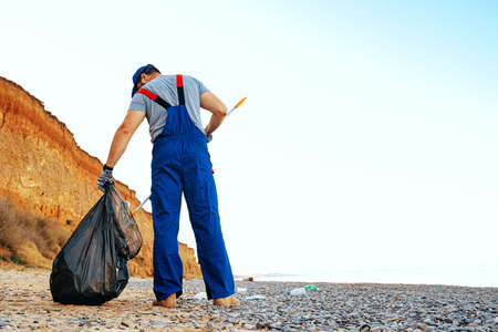 Man volunteer collecting garbage on the beach with a reach extender stickの写真素材
