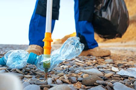 Close up photo of a man collecting garbage with a grabbing tool on the beachの写真素材