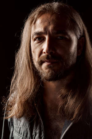 Long-haired masculine middle-aged man standing in the dark