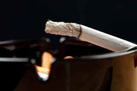 Burning cigarette in a black ash trayの写真素材