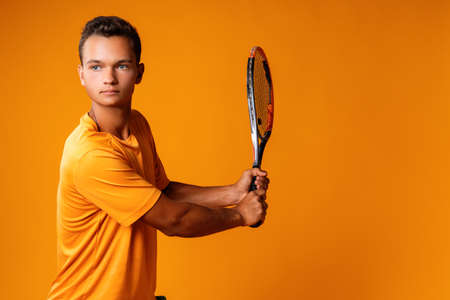 Studio shot of a young tennis player holding racket against orange backgroundの写真素材