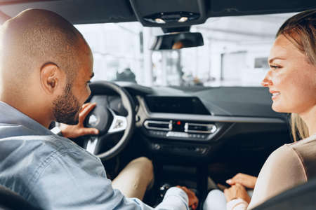 Joyful young couple looking around inside a new car they are going to buy in a car shop