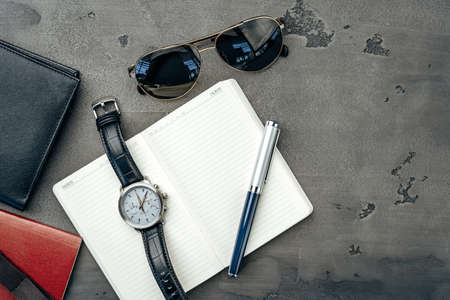 Businessmans accessories including notepad, watch and purse on dark grey background