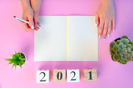 Female hands and handsof a kid holding 2021 Year wooden cubes above pink