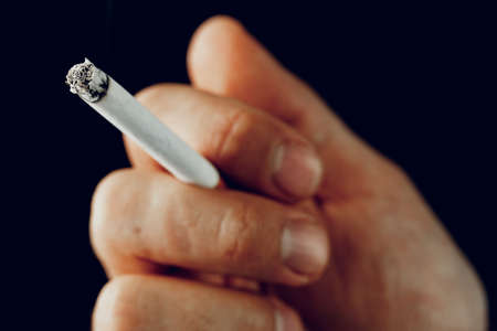 Male hand with a burning cigarette against black background
